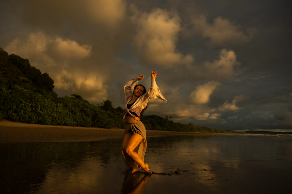 bohemian woman dancing on the beach at sunset with golden light and the water reflecting back at her